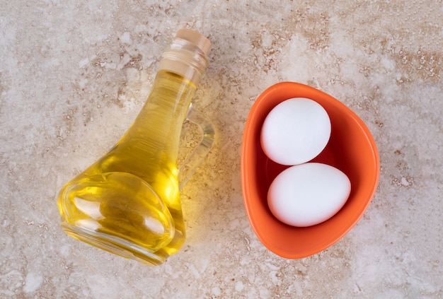 Dwa świeże białe jaja kurze w szklanej butelce oleju