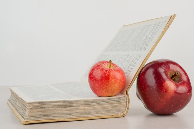 Dwa świeże jabłka z książką na białym stole.