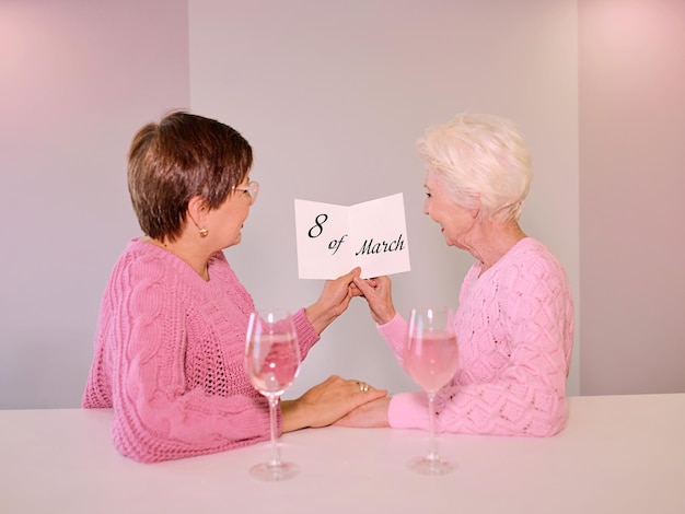Dwie dojrzałe kobiety pijące wino i dające pocztówkę święta przyjaźni kochają małżeństwa osób tej samej płci