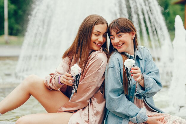 Dwie dziewczyny siedzą przy fontannie i idą lody.