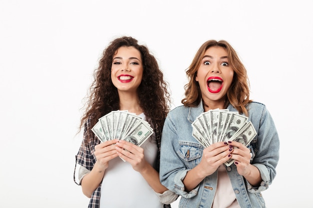 Bezpłatne zdjęcie dwie dziewczyny szczęśliwy gospodarstwa pieniądze i radują się z białej ściany