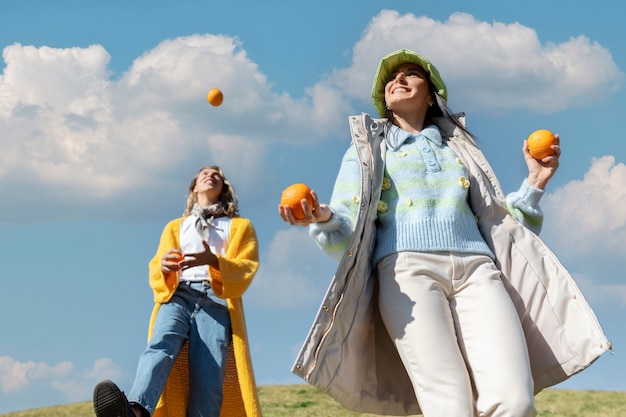 Bezpłatne zdjęcie dwie koleżanki bawiące się pomarańczami na polu pod gołym niebem