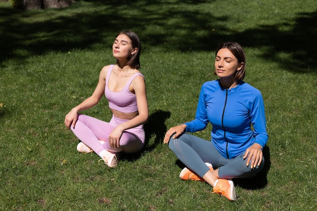 Dwie ładne kobiety w sporcie nosić na trawie w parku w słoneczny dzień robi jogi, złapać promienie słoneczne