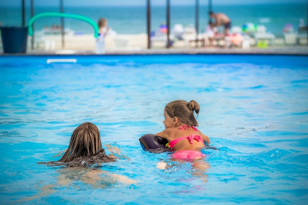 Dwie małe siostry dziewczynki pływają w dużym basenie z czystą, błękitną moją wodą w pobliżu hotelu, na tle morza i plaży. koncepcja wakacje tropikalny gorący kraj z dziećmi