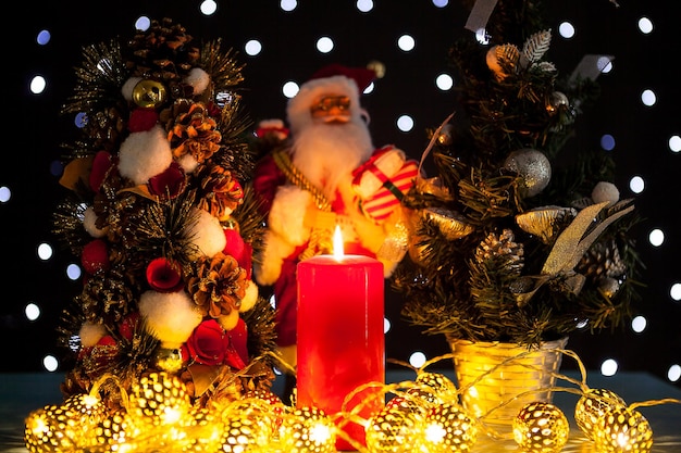 Dwie mini choinki i figurka Świętego Mikołaja na czarnym tle ze światłami bokeh