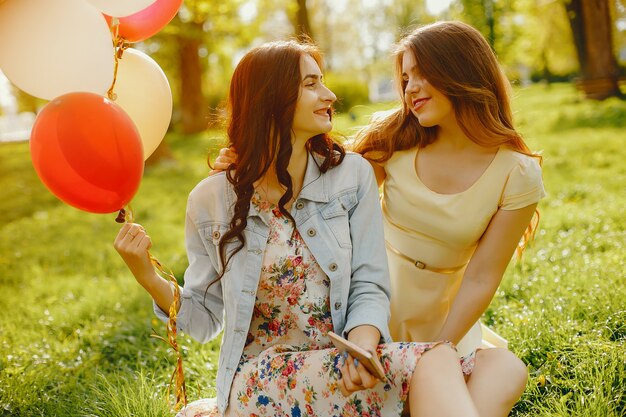 dwie młode i jasne dziewczyny spędzają czas w letnim parku z balonami