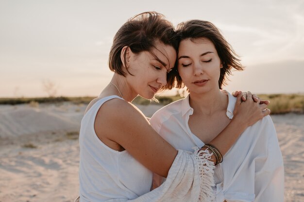 Dwie młode kobiety bawią się na plaży o zachodzie słońca, wesoły-lesbijka kochają romans