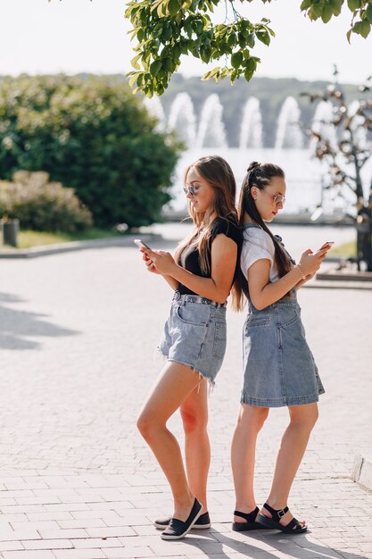 Dwie młode ładne dziewczyny na spacerze w parku z telefonami