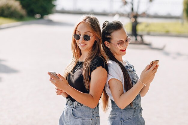 Dwie młode ładne dziewczyny na spacerze w parku z telefonami