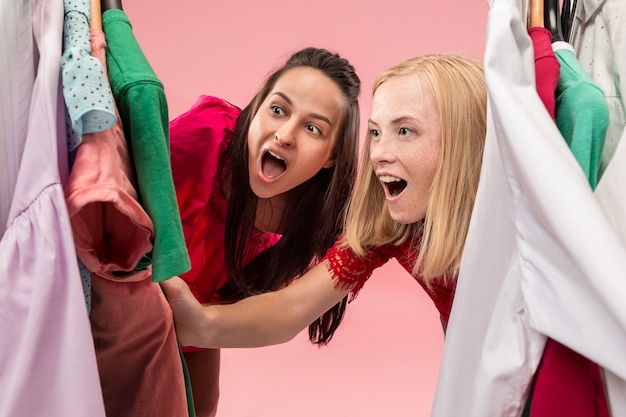 Dwie młode ładne dziewczyny patrzą na sukienki i przymierzają je, wybierając w sklepie