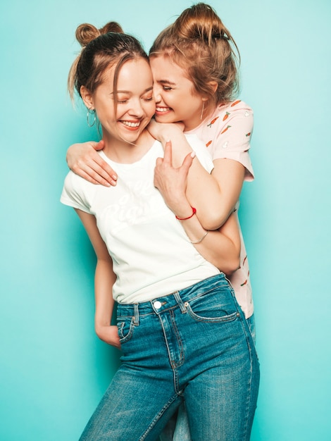 Dwie Młode Piękne Blond Uśmiechnięte Dziewczyny Hipster W Modne Letnie Hipster Jeans Ubrania. Seksowne Beztroskie Kobiety Pozuje Blisko Błękit ściany. Modne I Pozytywne Modele Zabawy