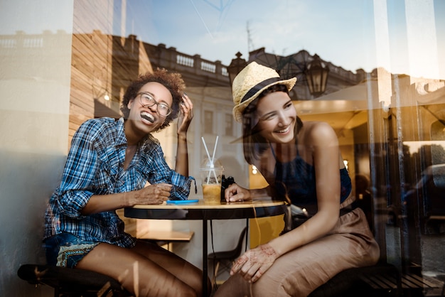 Bezpłatne zdjęcie dwie młode piękne dziewczyny uśmiechnięte, śmiejąc się, odpoczywając w kawiarni. strzał z zewnątrz.