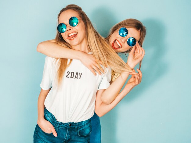 Dwie młode piękne uśmiechnięte blond hipster dziewczyny w modne letnie dżinsy spódnice ubrania.