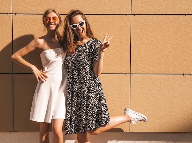 Dwie młode piękne uśmiechnięte hipster dziewczyny w modnej letniej sukience.
