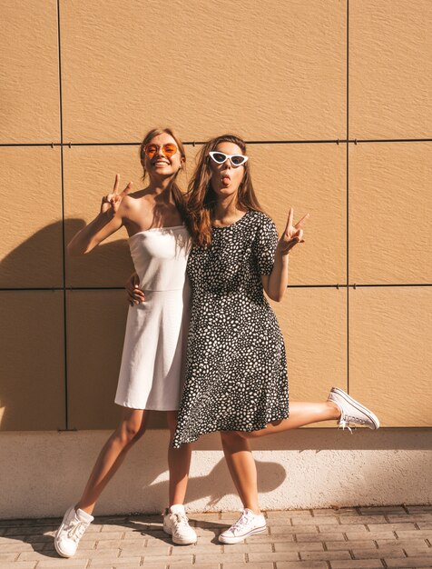 Dwie młode piękne uśmiechnięte hipster dziewczyny w modnej letniej sukience.