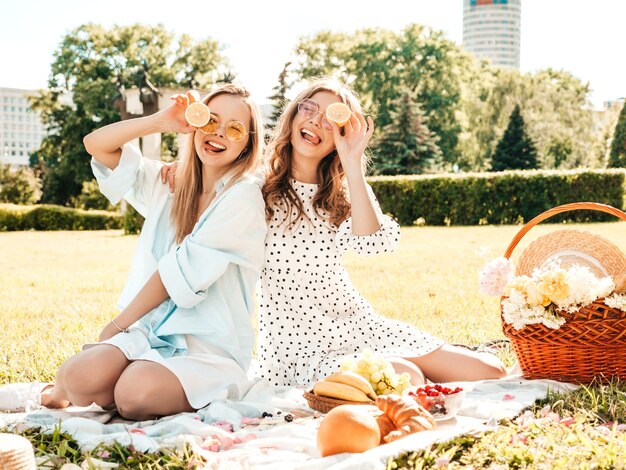 Dwie młode piękne uśmiechnięte kobiety w modnej letniej sukience i kapeluszach. Beztroskie kobiety robią piknik na zewnątrz.
