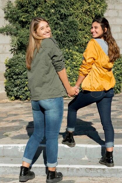 Dwie nastoletnie dziewczyny trzymając się za rękę, patrząc przez ramię na zewnątrz