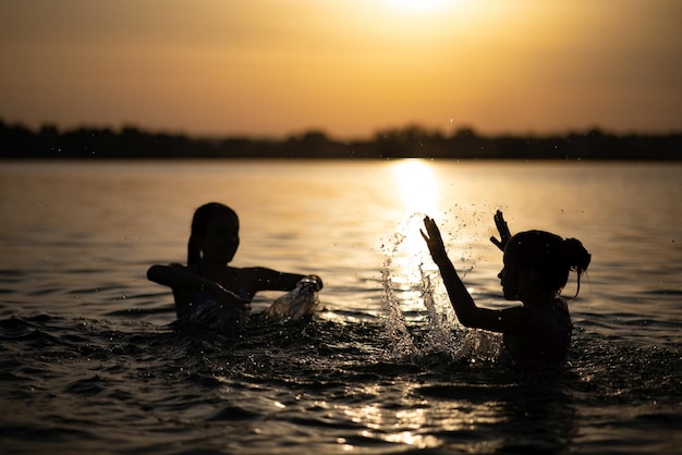 Dwie siostry pluskające się w wodzie bawiące się w jeziorze na tle zachodu słońca