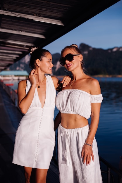 Dwie stylowe kobiety w białe letnie ubrania w pobliżu morza o zmierzchu