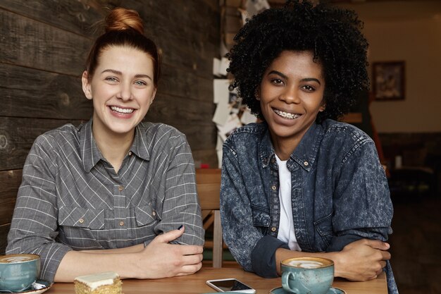 Dwie szczęśliwe lesbijki piją kawę, siedząc przy stole w przytulnej restauracji