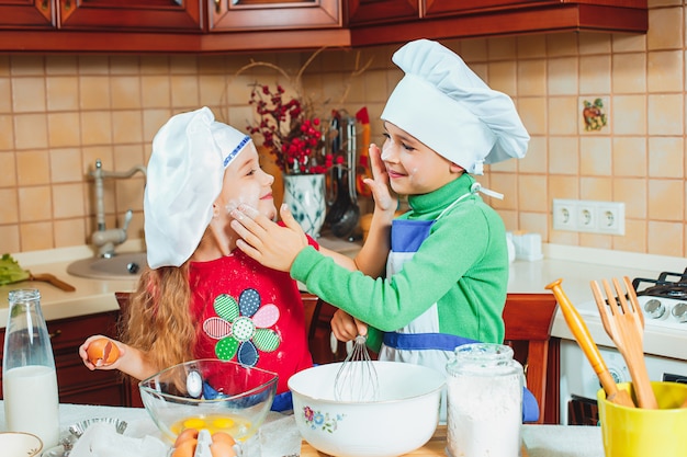 Dwie szczęśliwe zabawne dzieciaki przygotowują ciasto, pieczą ciasteczka w kuchni