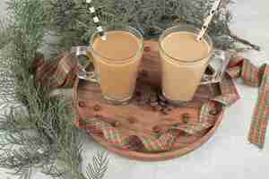Bezpłatne zdjęcie dwie szklanki kawy ze słomkami i wstążką na drewnianym talerzu