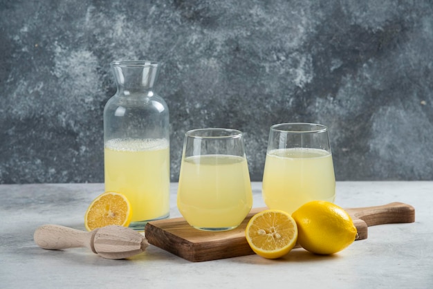 Bezpłatne zdjęcie dwie szklanki soku z cytryny i słoik na drewnianej desce.