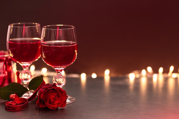 Dwie szklanki wina i czerwona róża na niewyraźnym tle z bokeh