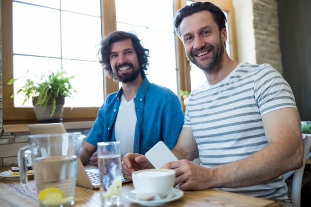Dwie uśmiechnięte mężczyzn siedzących przy stole w kawiarni