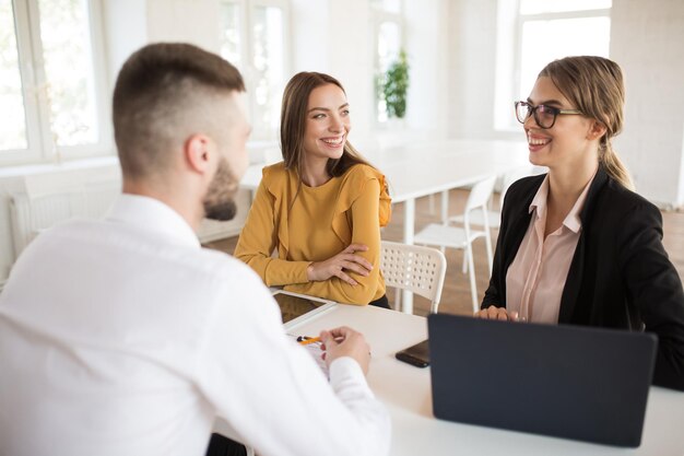 Dwie wesołe kobiety biznesu szczęśliwie rozmawiające z mężczyzną ubiegającym się o pracę Młodzi uśmiechnięci pracodawcy spędzający rozmowę kwalifikacyjną w nowoczesnym biurze