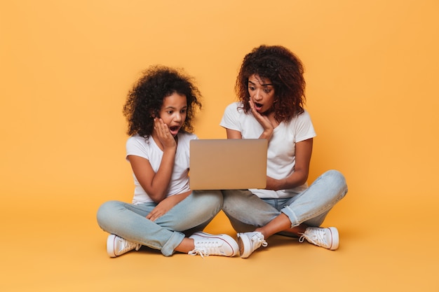 Dwie zdziwione afro amerykańskie siostry używa laptopu
