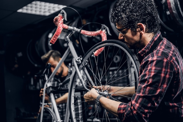 Bezpłatne zdjęcie dwóch atrakcyjnych mechaników naprawia zepsuty rower w swoim ciemnym warsztacie.