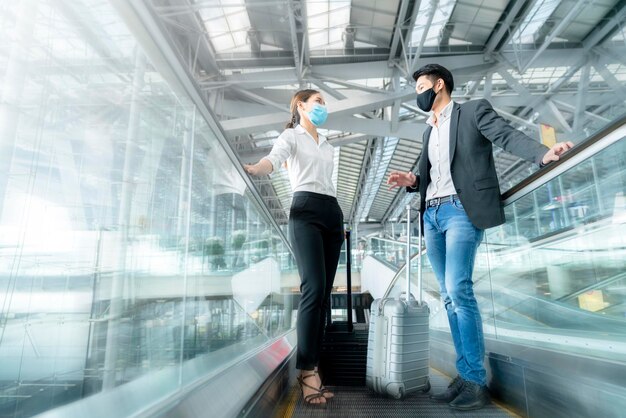 Dwóch azjatyckich partnerów biznesowych z ochroną maski na twarz dystans społeczny nowy normalny styl życia Podróżujący w interesach chodzący na lotnisku z ruchem bagażu