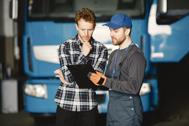 Dwóch facetów rozmawia o pracy. Pracować w garażu w pobliżu ciężarówki. Przekazywanie dokumentów wraz z towarem