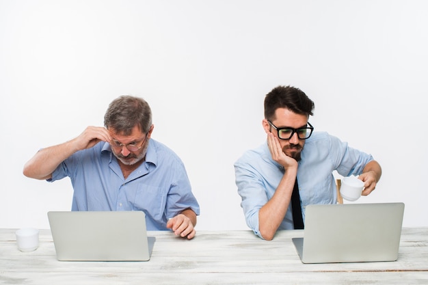 Dwóch kolegów pracujących razem w biurze na białym tle. obaj patrzą na ekrany komputerów. pojęcie negatywnych emocji i złych wiadomości