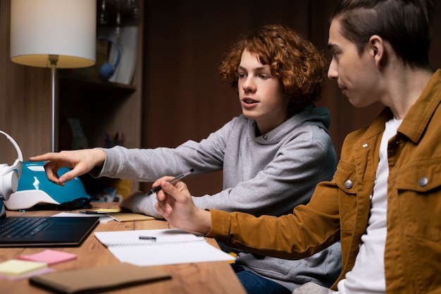 Dwóch nastoletnich chłopców uczących się razem w domu z laptopem