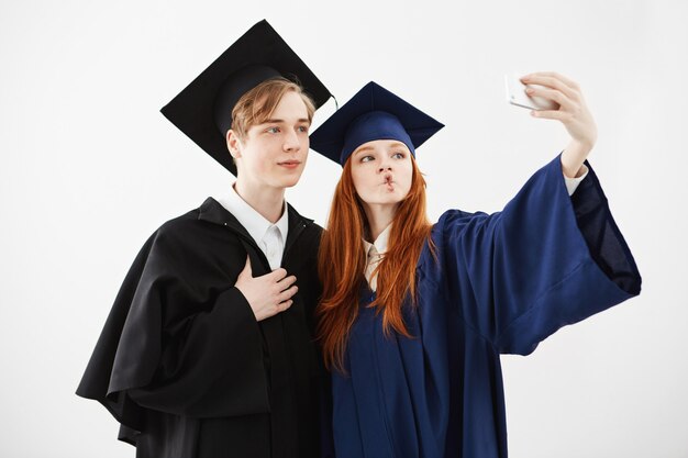 Dwóch szczęśliwych absolwentów uniwersytetu wygłupiać, robiąc selfie.