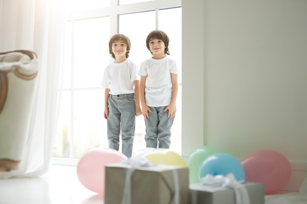 Dwóch uroczych latynoskich bliźniaków, małe dzieci w strojach codziennych, wyglądające na szczęśliwych, witające się z rodzicami, przygotowujące dla nich kolorowe balony i pudełka na prezenty. święta, prezenty, koncepcja dzieciństwa