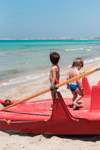 Dwoje dzieci na plaży stoi na łodzi wiosła