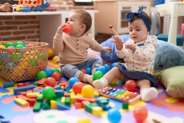 Dwoje małych dzieci bawiących się piłkami i ksylofonem siedzi na podłodze w przedszkolu