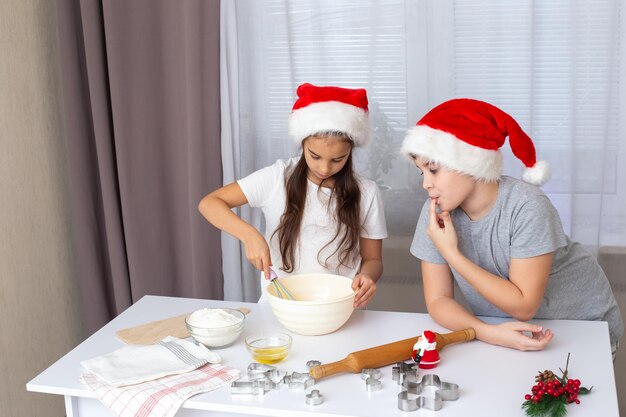 Dwoje szczęśliwych dzieci, brat i siostra w czerwonych czapkach, przygotowują świąteczne ciasteczka w kuchni