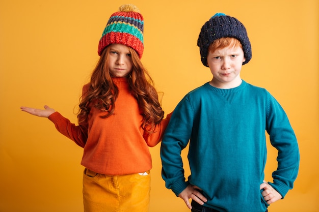 Dwoje zdezorientowanych małych rudych dzieci w ciepłych kapeluszach.