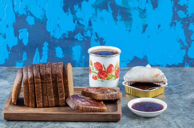 Bezpłatne zdjęcie dżem truskawkowy z kromką ciemnego chleba i filiżanką herbaty.