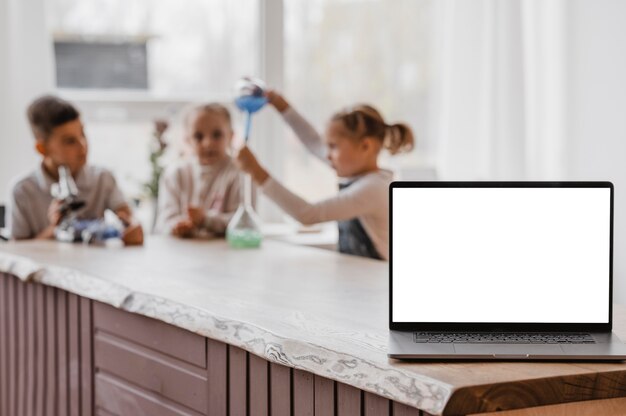 Dzieci bawiące się elementami chemii obok laptopa z pustym ekranem