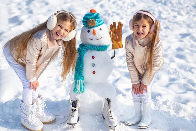 Dzieci lepią bałwana na białym tle śniegu, robiąc bałwana i zimową zabawę dla dzieci
