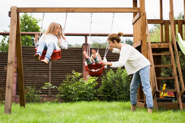 Bezpłatne zdjęcie dzieci na huśtawce. dziewczęce siostry kołyszą się na huśtawce na podwórku. letnia zabawa.