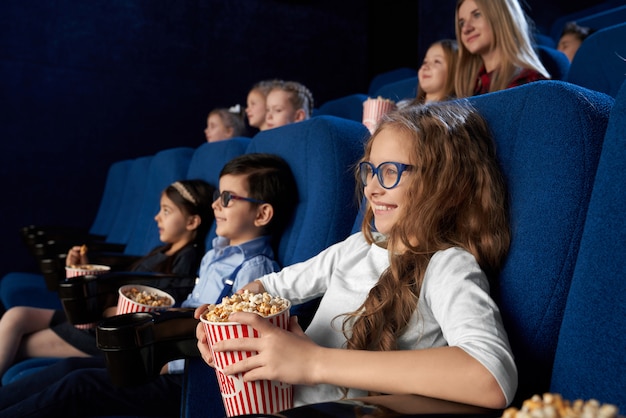 Dzieci oglądają film w kinie, trzymając wiadra popcornu.