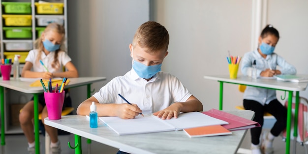 Dzieci piszą w klasie w maskach medycznych