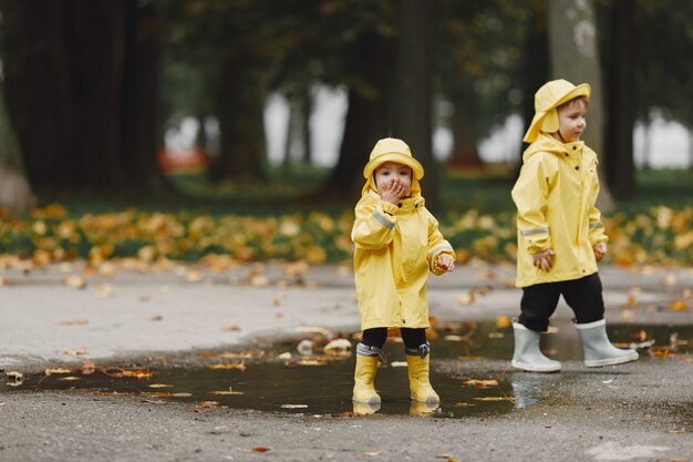 Dzieci w jesiennym parku. Dzieci w żółtych płaszczach przeciwdeszczowych. Ludzie bawią się na świeżym powietrzu.