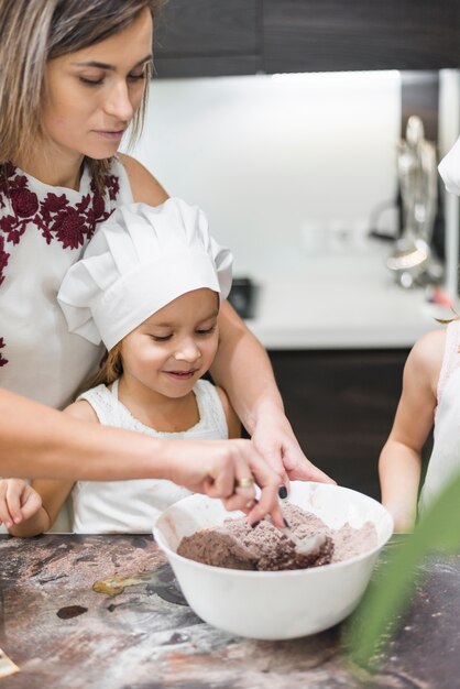 Dzieciaki stoi przed matką podczas gdy mieszający kakaowego proszek w pucharze na upaćkanym kuchennym kontuarze